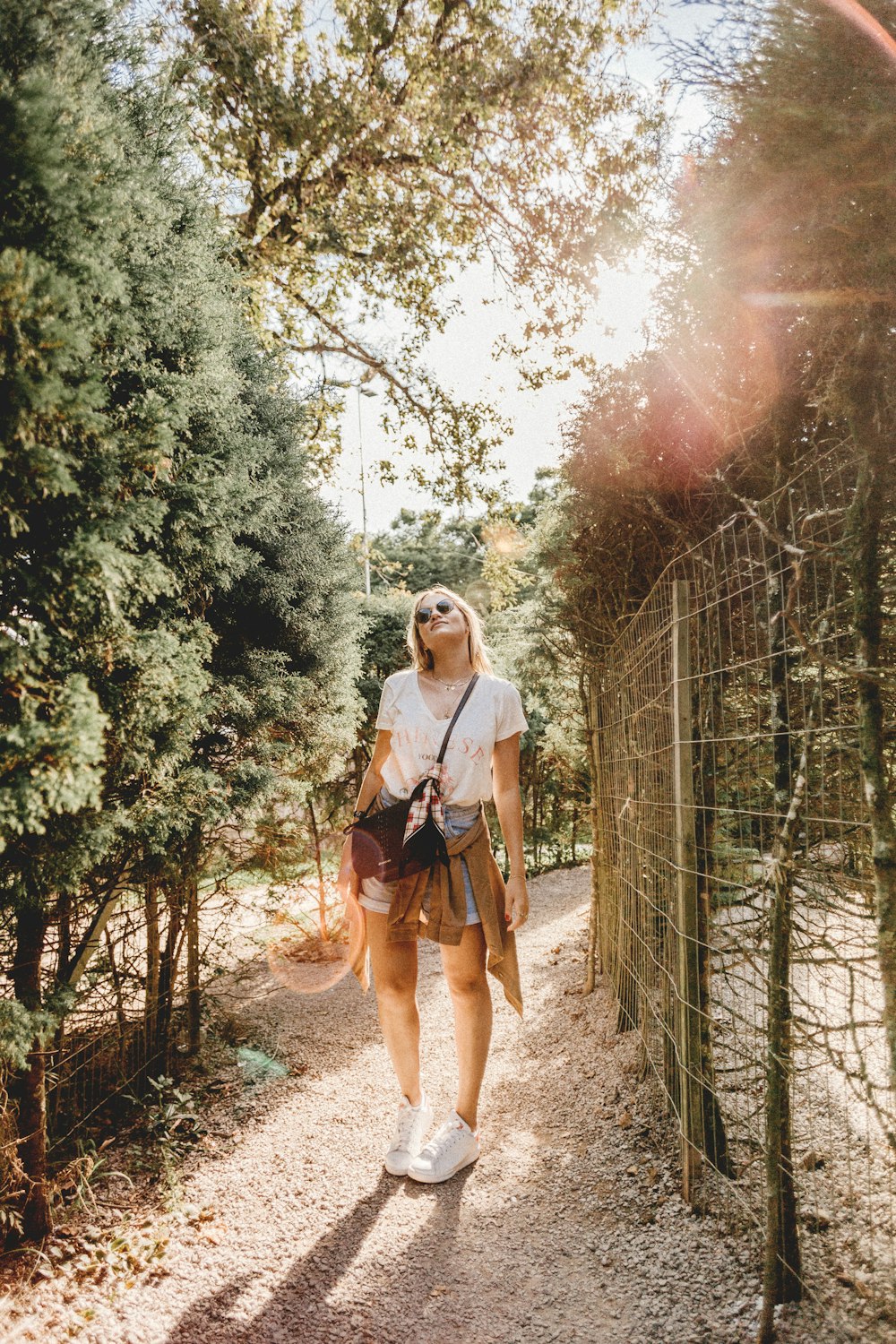 femme debout portant un t-shirt blanc debout entre la clôture et les arbres regardant vers le haut