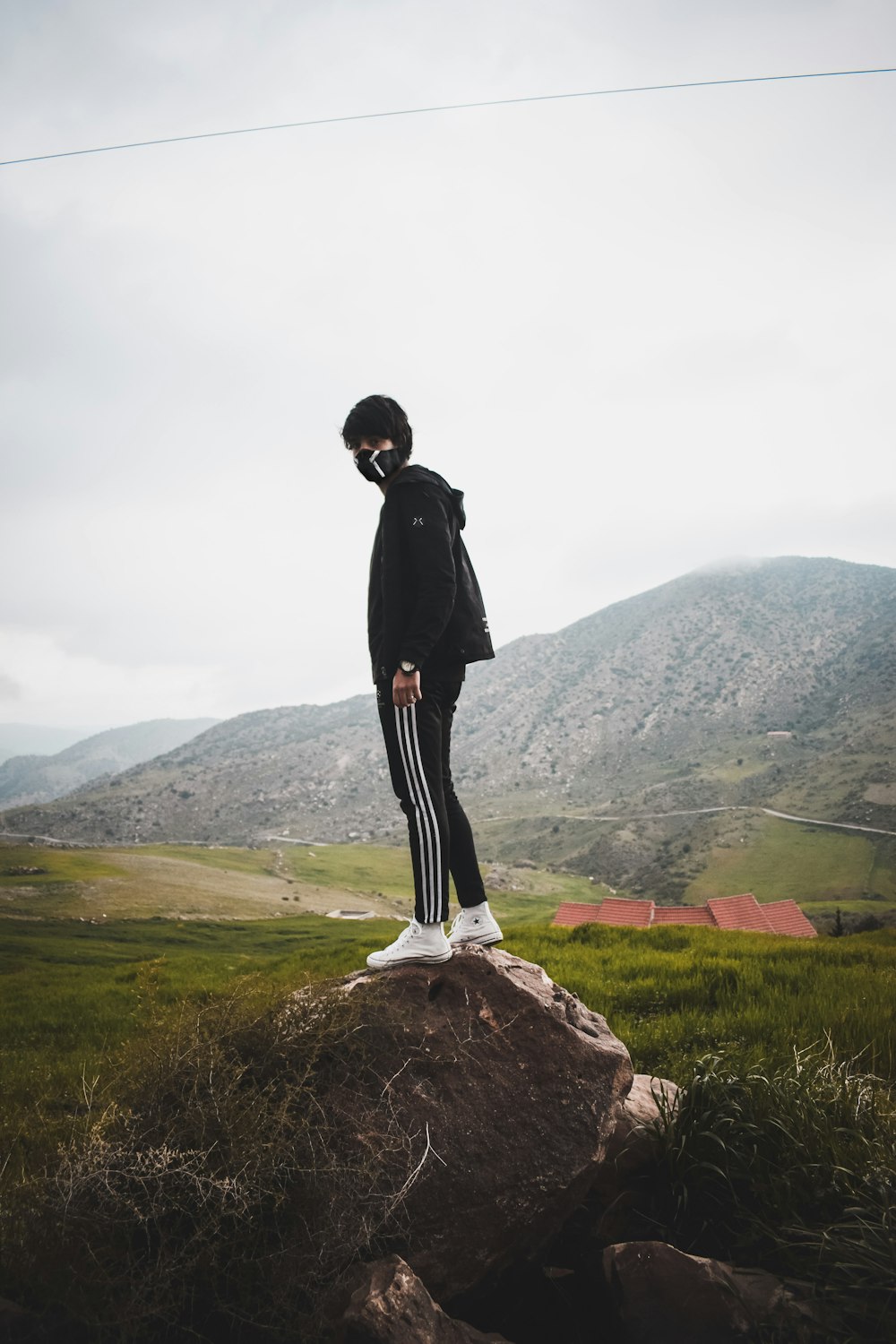 man in black jacket and black track pants standing on rock