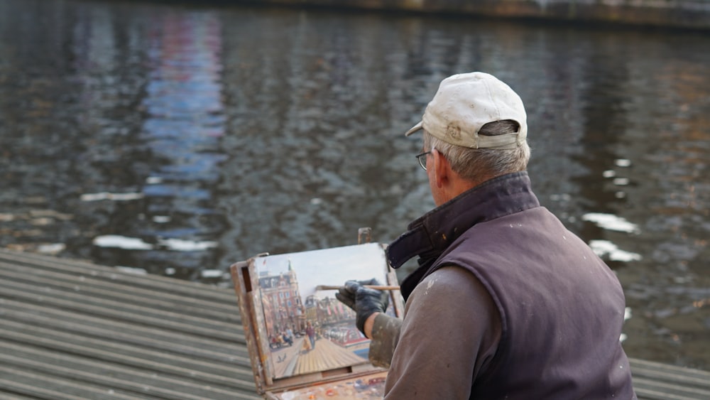 man painting near the body of water during daytime
