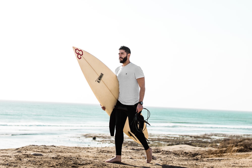 man walking at the sea while holding surfboard