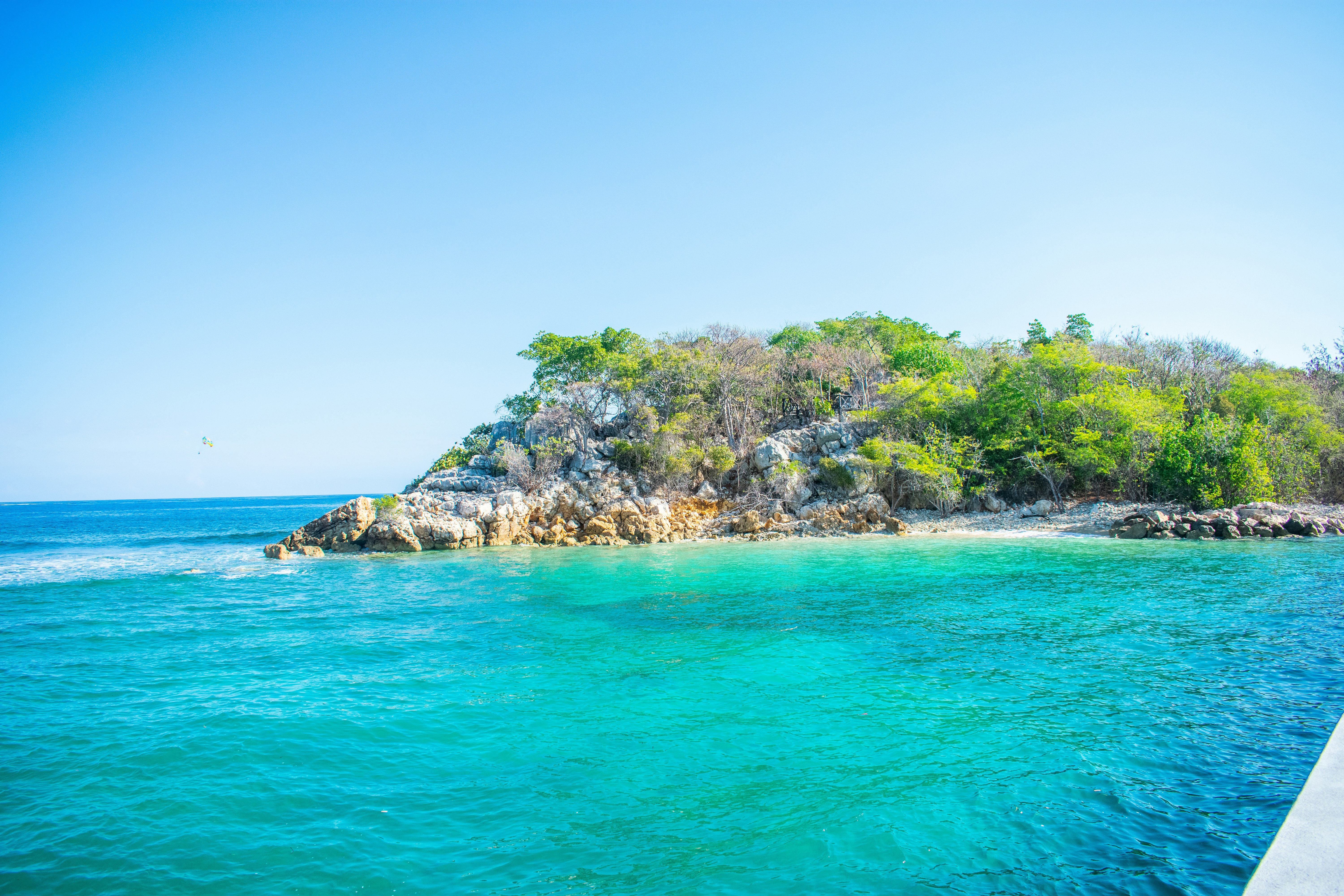 calm sea near rock formation surrounded with trees under blue sky