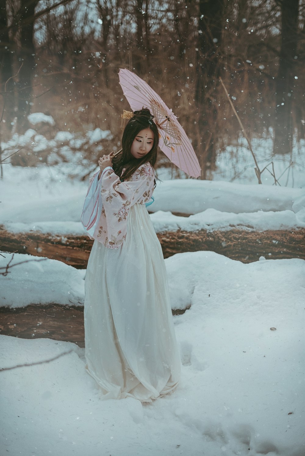 雪の中で傘を持つ白いドレスを着た女性