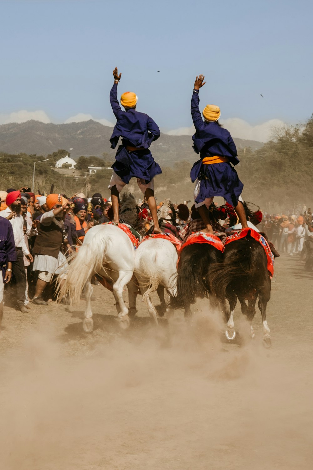 Dos personas de pie en caballos blancos rodeados de gente