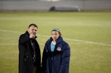 A woman wearing a cozy coat and scarf standing on a sports field.