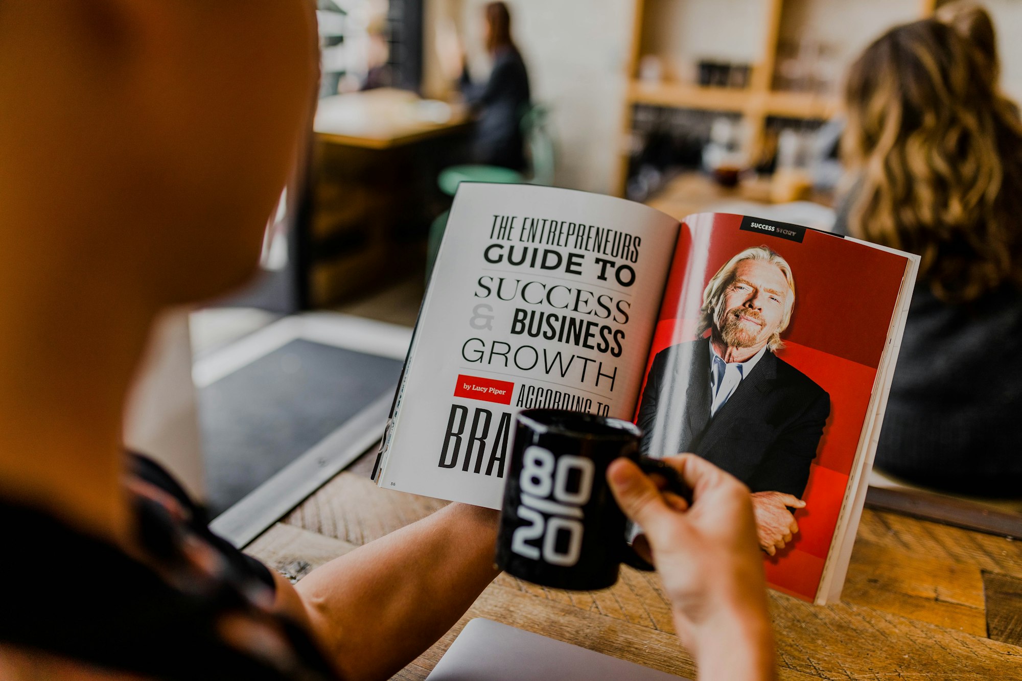 someone reading a book on entrepreneurship and success, holding a coffee mug reading "80/20"