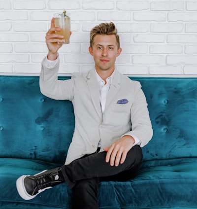 man in gray blazer raising drinking glass while sitting on sofa