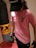 A person wearing a pink T-shirt and a black cap is holding a dumbbell in one hand. They are standing next to a punching bag, suggesting a fitness or gym setting.