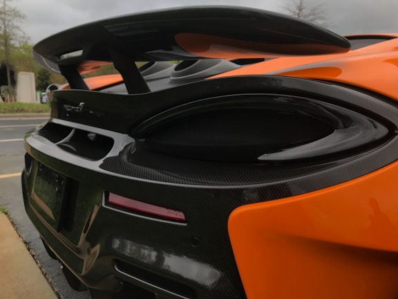 Close-up of a sleek, 3D-printed carbon fiber rear wing mounted on a C8 Corvette under bright California sunlight.