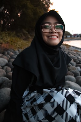 A serene woman in hijab sitting peacefully by a mountain lake during sunrise.