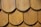 Close-up of a wooden shingle roof with overlapping, semi-circular tiles displaying a natural wood grain pattern. The shingles are arranged in a uniform pattern, indicating craftsmanship and durability.