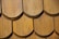 Close-up of a wooden shingle roof with overlapping, semi-circular tiles displaying a natural wood grain pattern. The shingles are arranged in a uniform pattern, indicating craftsmanship and durability.