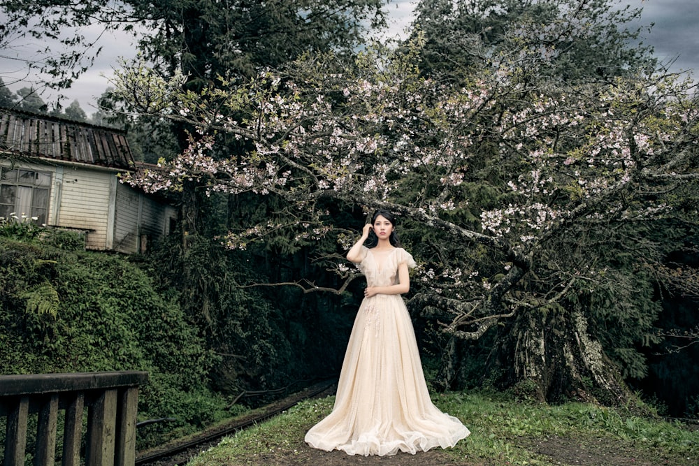 woman standing beside trees wearing white dress during daytime