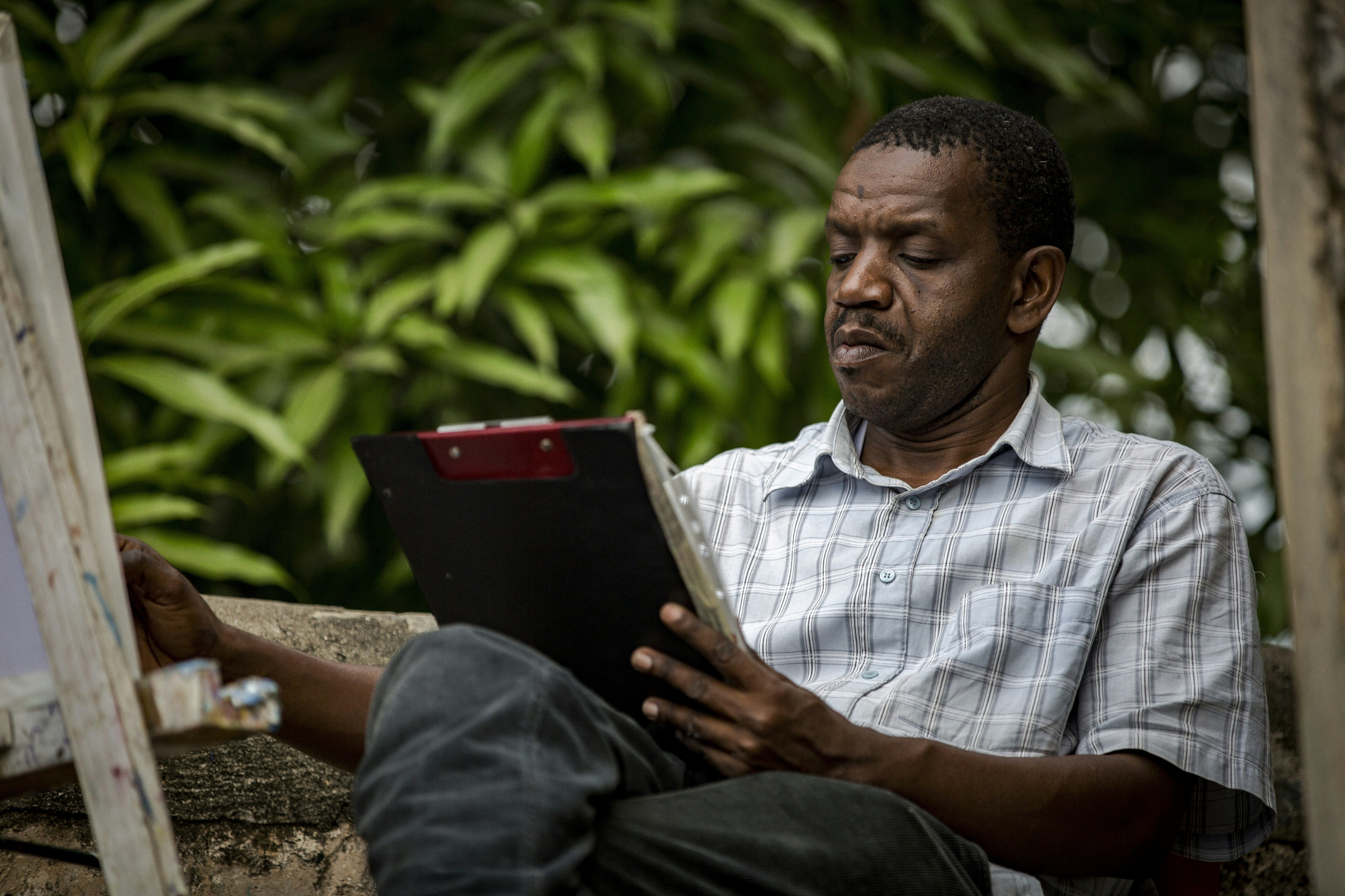 man holding paper siting near green tree