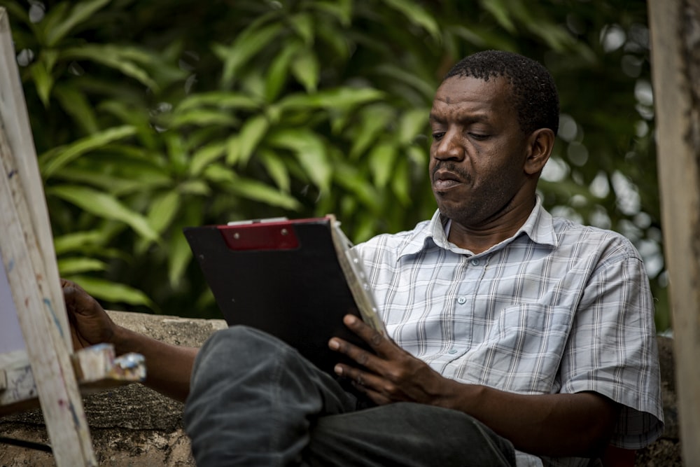 man holding paper siting near green tree