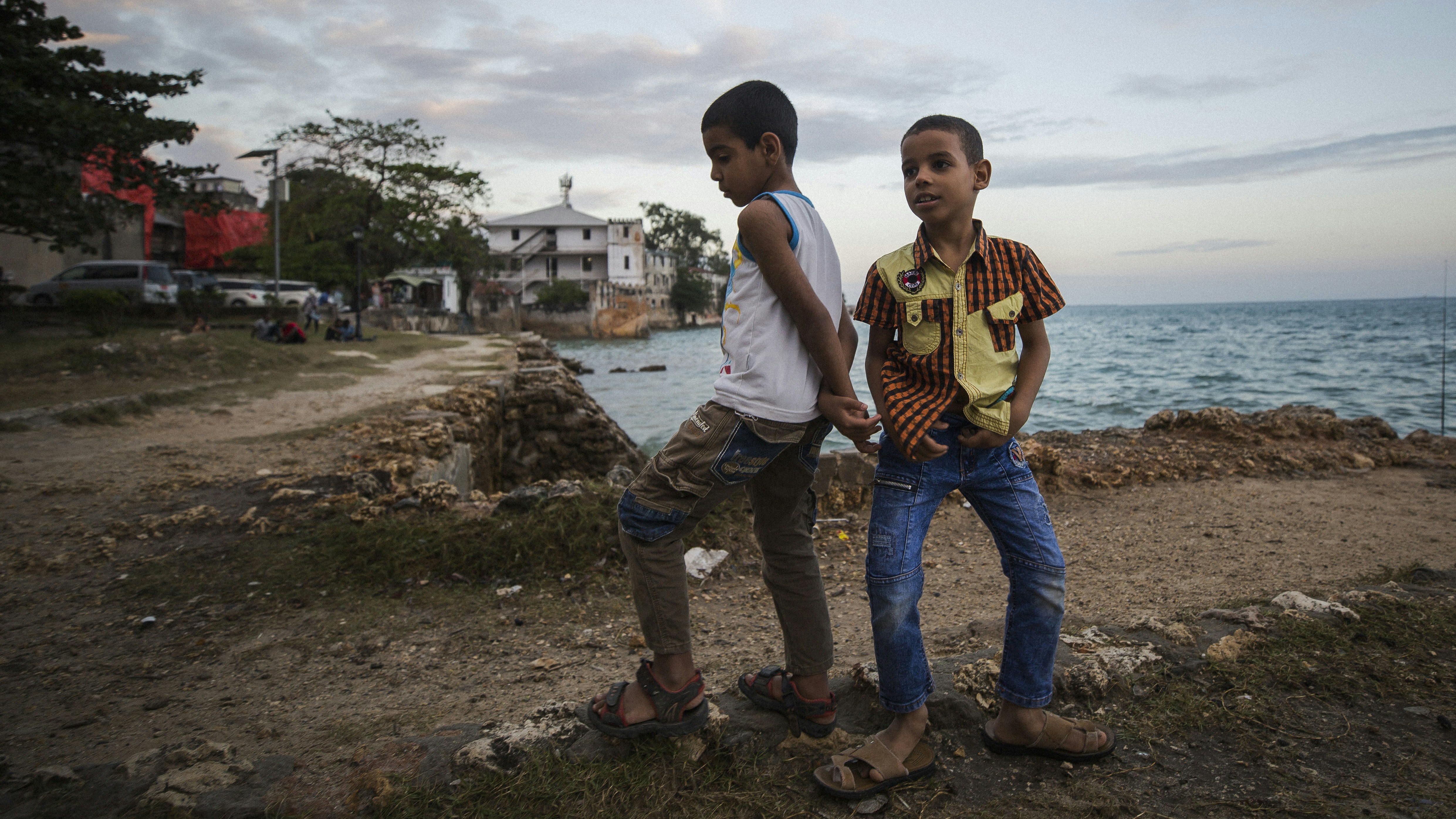 two boy standing on brown soil near body of water
