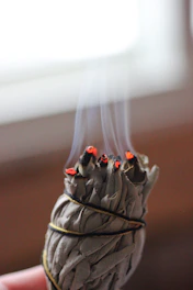 Close-up of natural sage bundle burning with soft smoke curling upwards in a dark setting.