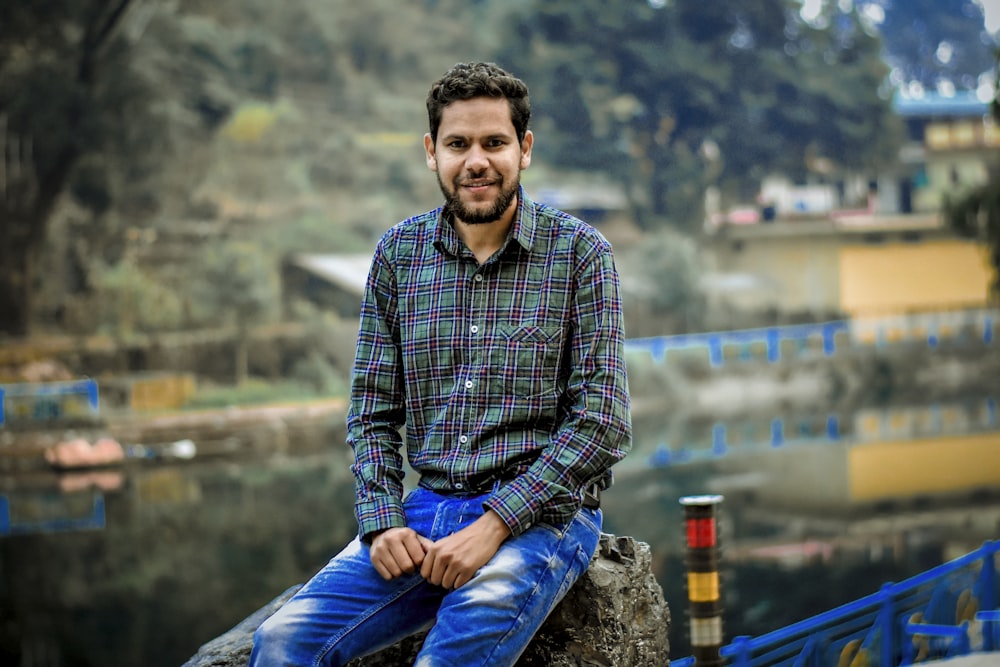 man sitting on rock near body of water