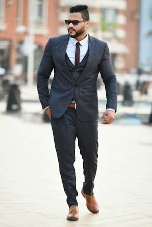 A stylish man in a tailored charcoal suit walking confidently through a sunlit city street.