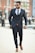 A well-dressed man confidently walking in an urban setting, showcasing a stylish outfit.
