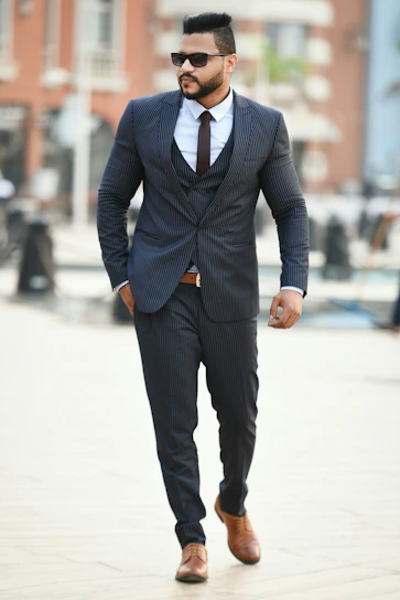 A stylish man wearing a tailored navy blue suit walking confidently in a modern city street.
