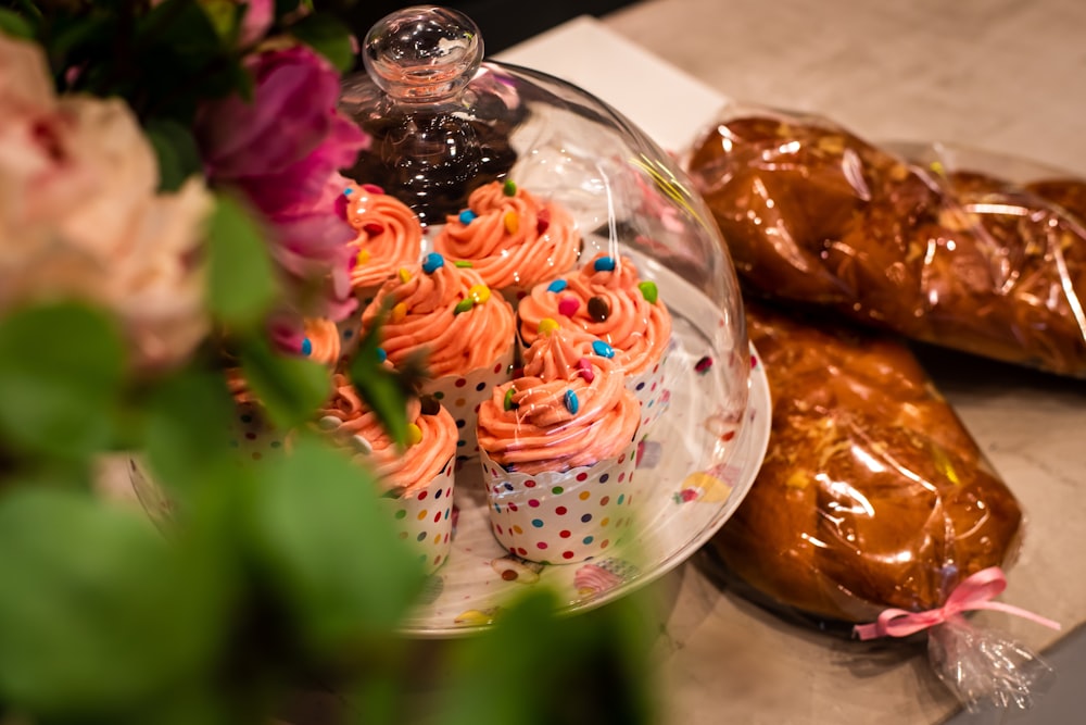 cupcakes with icing in clear glass cake dome on table