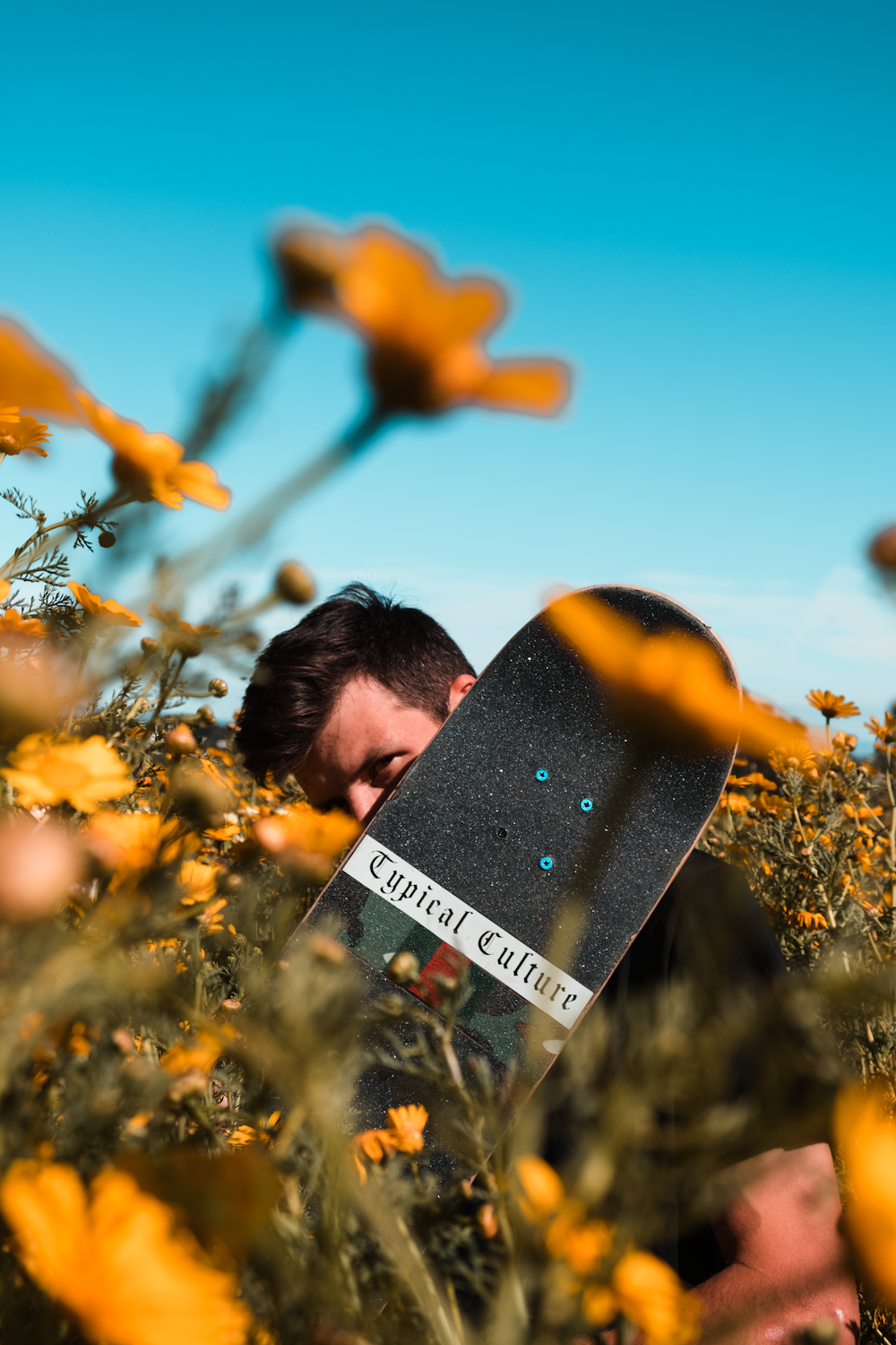 man hiding on skateboard near flower field