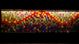 A vibrant wall display made up of numerous rectangular tiles arranged in a mosaic pattern, featuring a variety of colors including red, blue, yellow, and green. The tiles create an abstract, pixelated artwork with a complex design.