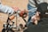 Several individuals are engaged in a hands-on activity focusing on mechanical equipment. The setup includes a metal pipe clamped into a red pipe threading tool, which is mounted on a tripod. Nearby, various tools and a canister are scattered on the ground. The background features an outdoor setting with dry, brown soil.