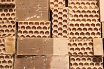 Several blocks of honeycomb-patterned beeswax are stacked closely together, displaying a textured surface with visible hexagonal impressions. The beeswax appears slightly rough, with some minor debris scattered throughout.