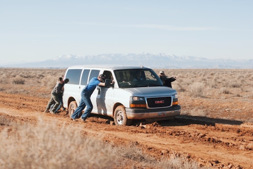men pushing white GMC van that is stuck