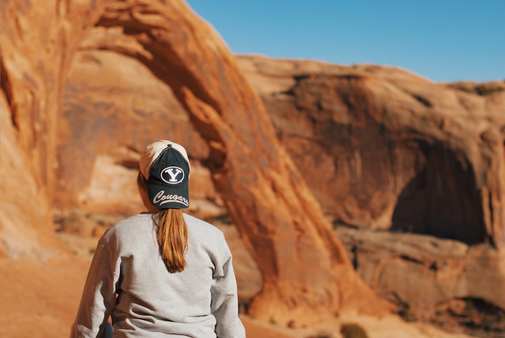 a woman wearing a hat standing in front of a rock formation