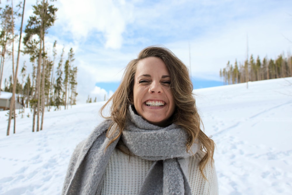 Mujer con pañuelo gris de pie nieve y sonriendo durante el día