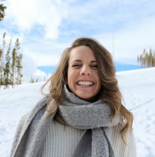 woman wearing gray scarf standing snow and smiling during daytime