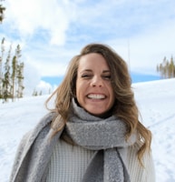 woman wearing gray scarf standing snow and smiling during daytime