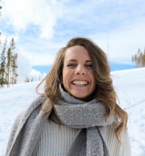 woman wearing gray scarf standing snow and smiling during daytime