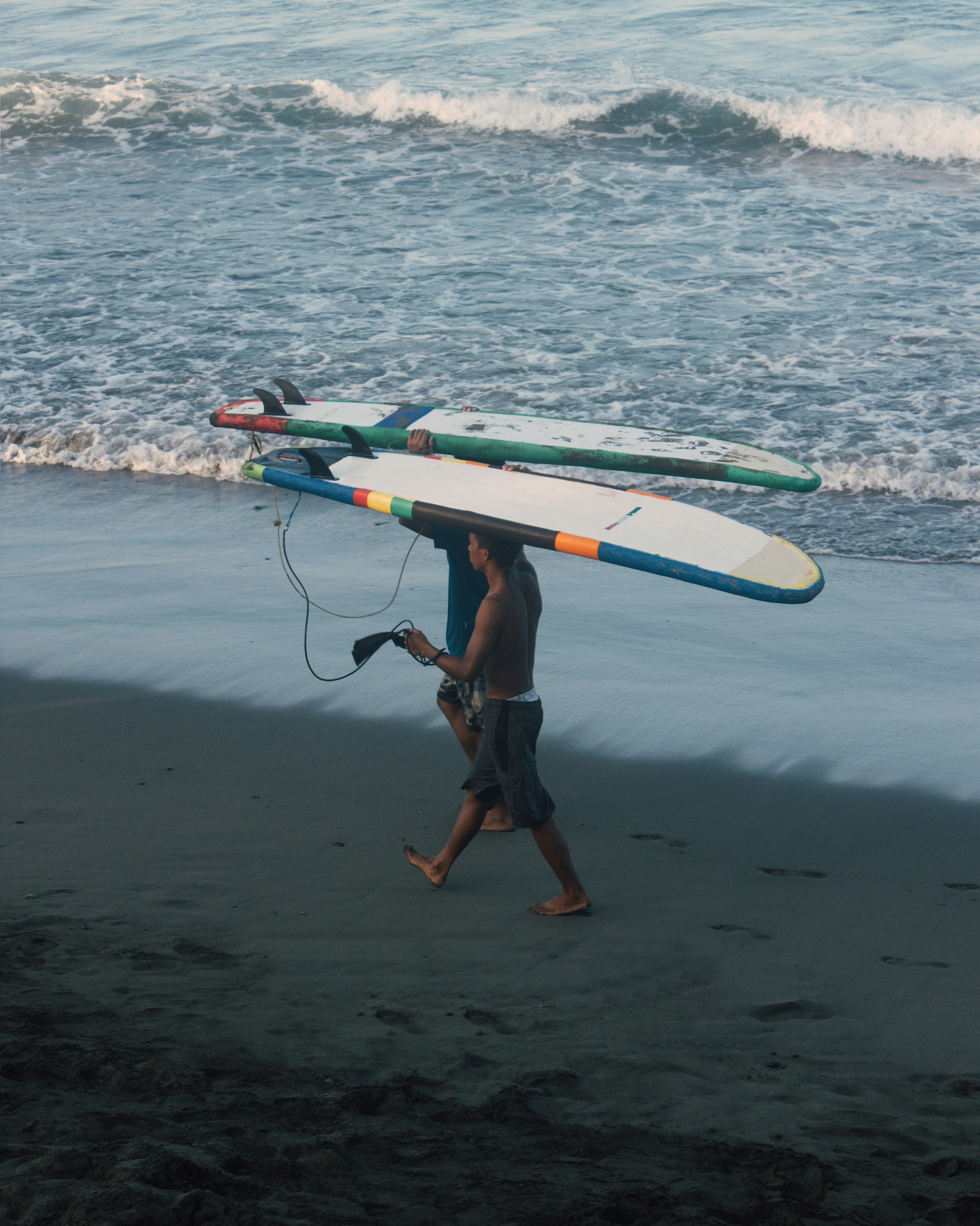 A person carrying a delivery box along a sandy beach with waves gently crashing in the background.