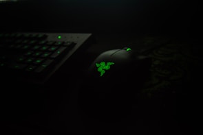 A dark-themed setup featuring a black computer mouse with a glowing green logo, placed next to a keyboard with illuminated green keys.
