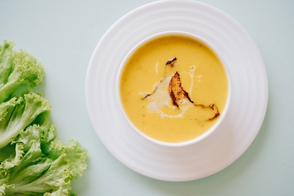 a white bowl filled with soup next to a leaf of lettuce