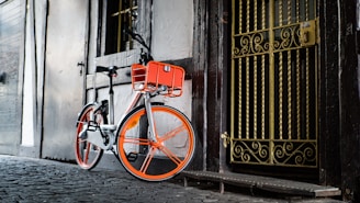A bright white and orange bicycle parked in front of a modern home.