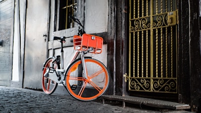 A bright white and orange bicycle parked in front of a modern home.