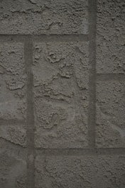 A textured concrete wall with a rough, unfinished surface featuring rectangular patterns typical of blocks or panels.