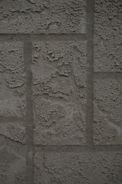 A textured concrete wall with a rough, unfinished surface featuring rectangular patterns typical of blocks or panels.