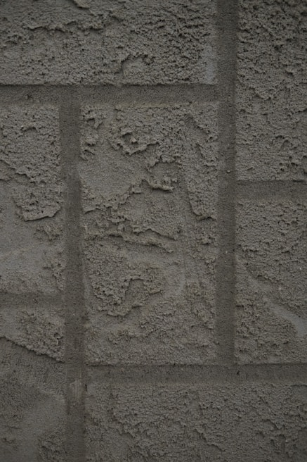 A textured concrete wall with a rough, unfinished surface featuring rectangular patterns typical of blocks or panels.