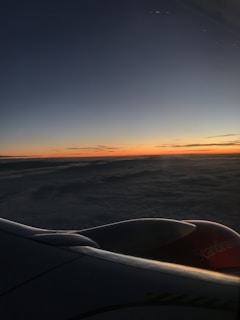 A serene sunset view from a plane window, with the horizon glowing in warm orange and blue hues.