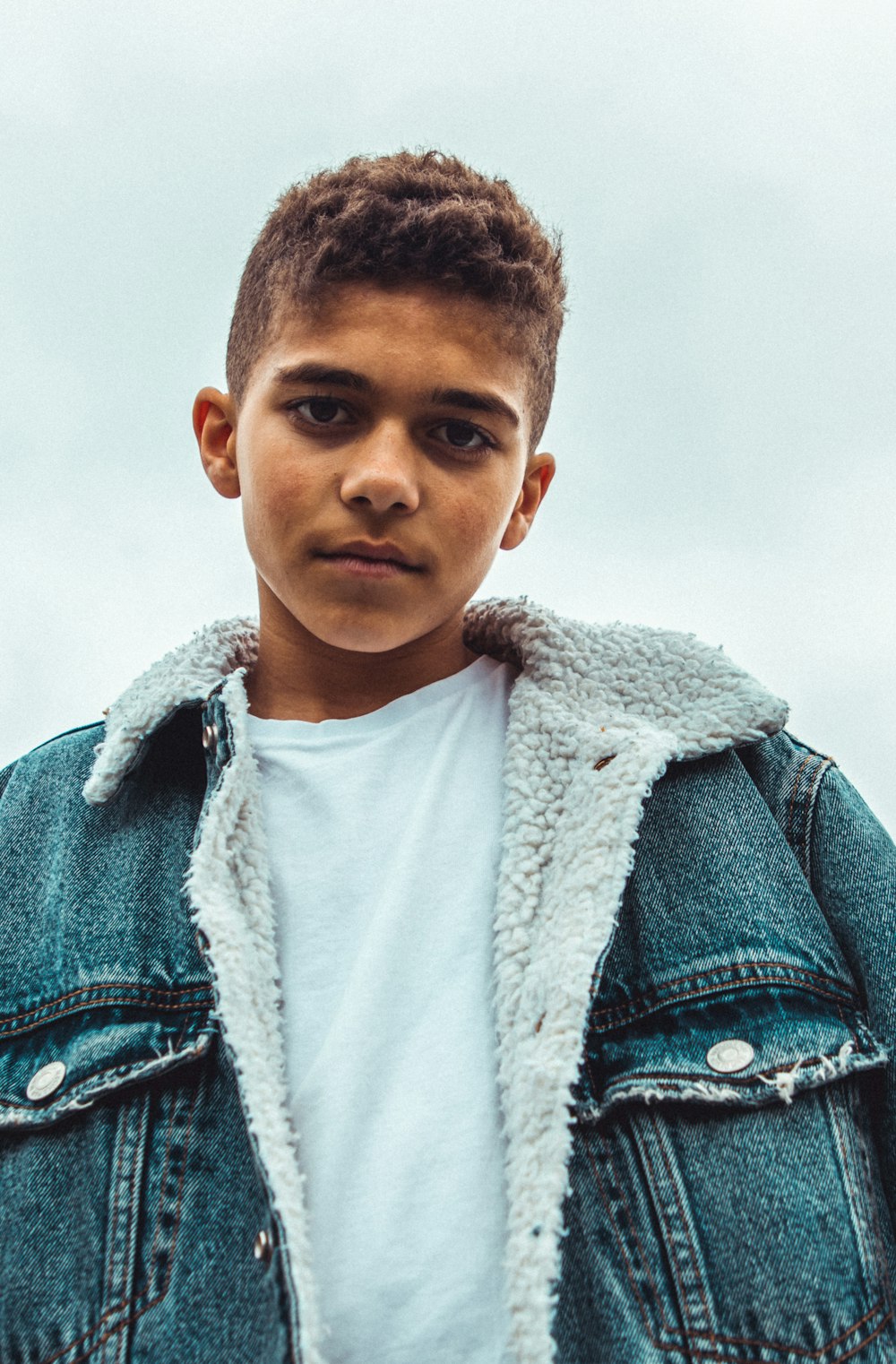 boy wearing blue denim jacket standing and looking straight