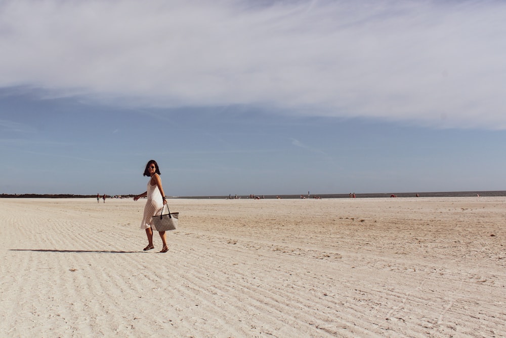 woman in white dress walking on sand during daytime