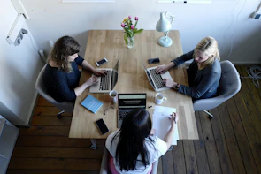 three women sitting around table using laptops