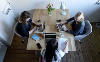 three women sitting around table using laptops