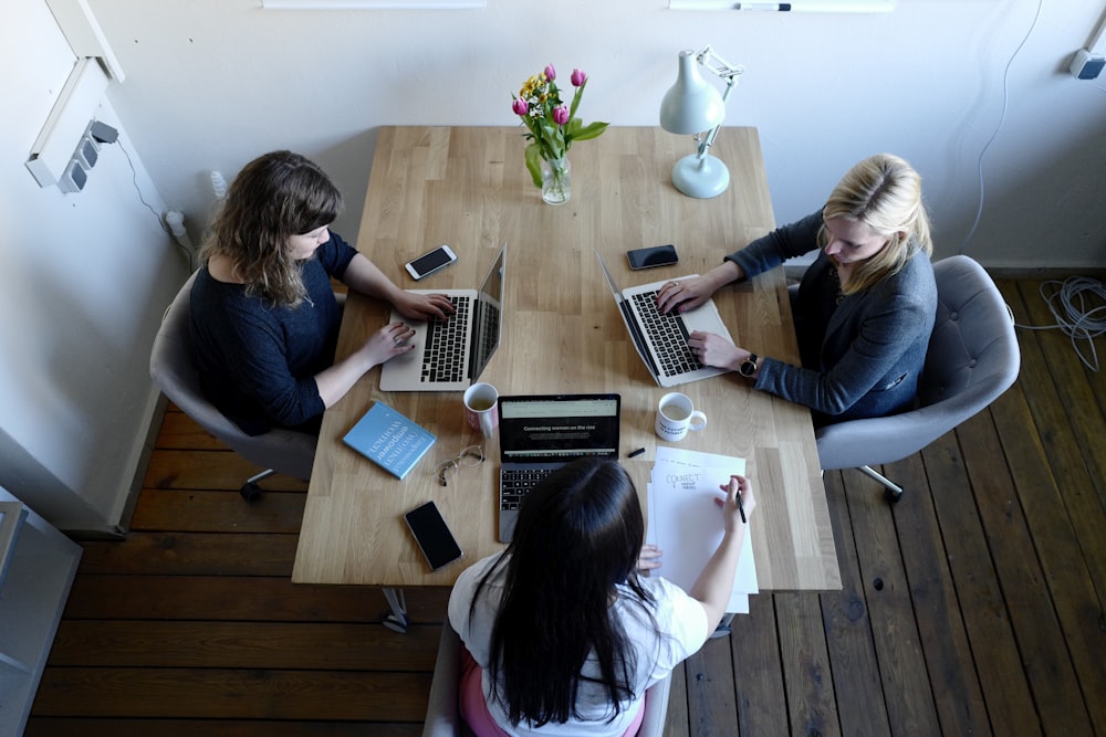 três mulheres sentadas ao redor da mesa usando laptops