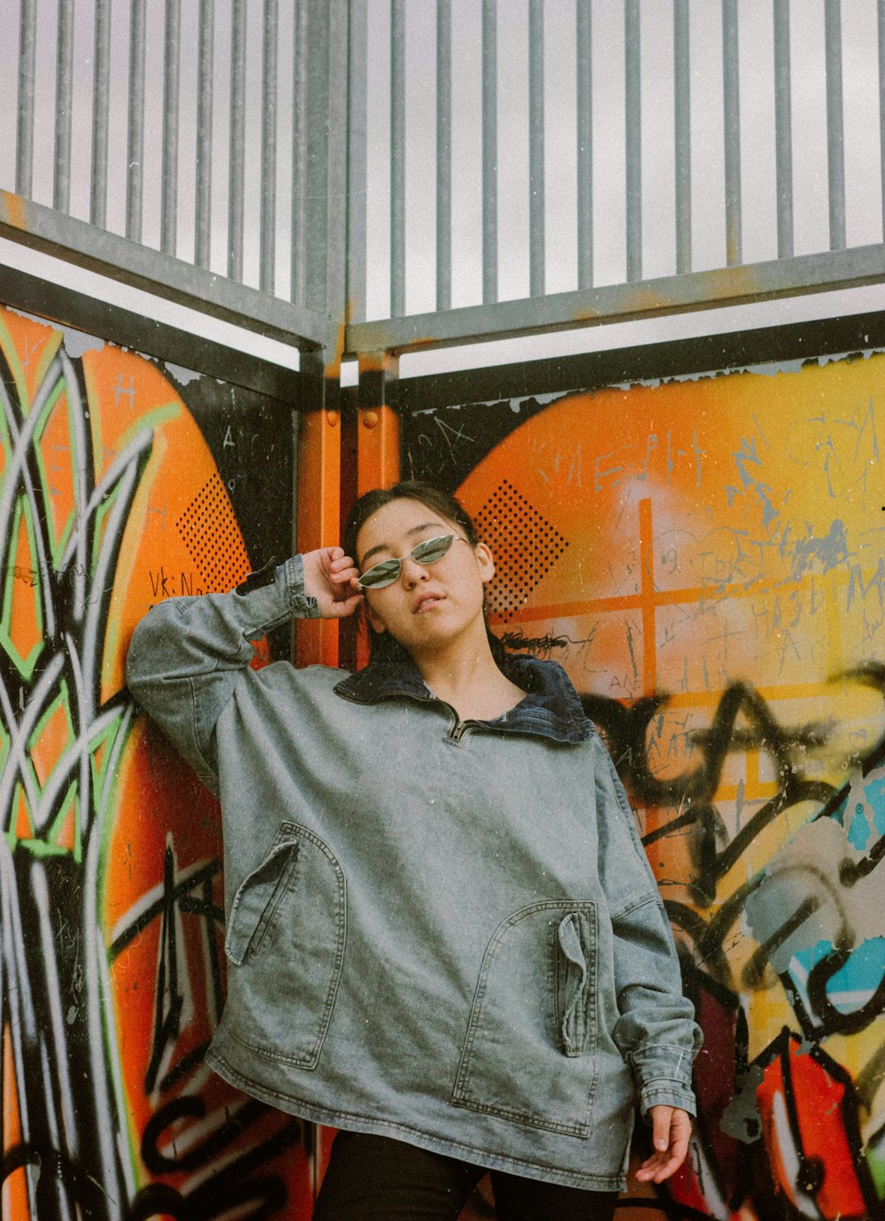 woman wearing gray jacket standing at graffiti painted wall